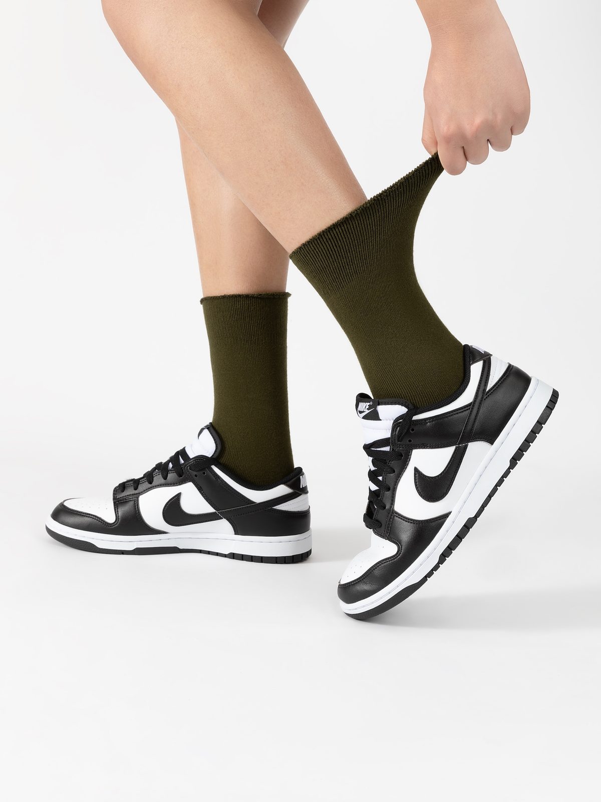 Olive crew socks worn with black-and-white sneakers, showing the cuff being gently stretched